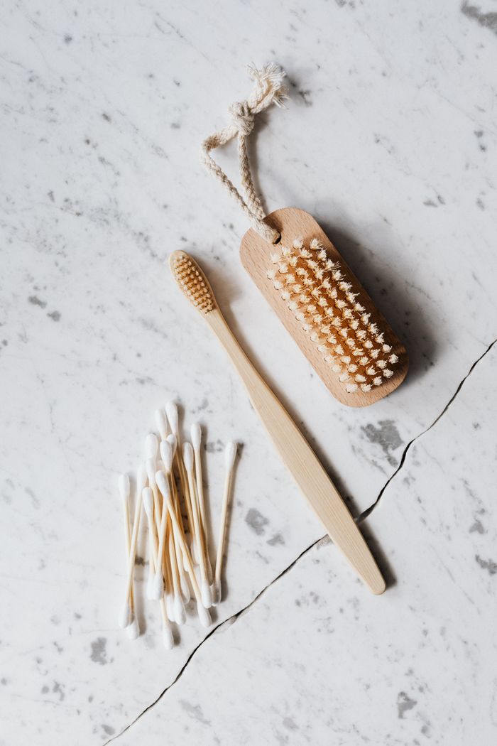Vue de dessus d’une brosse de nettoyage en bois et d’un coton-tige posés sur une surface en marbre, près d’une brosse à dents en bois sur fond de ligne de coupe